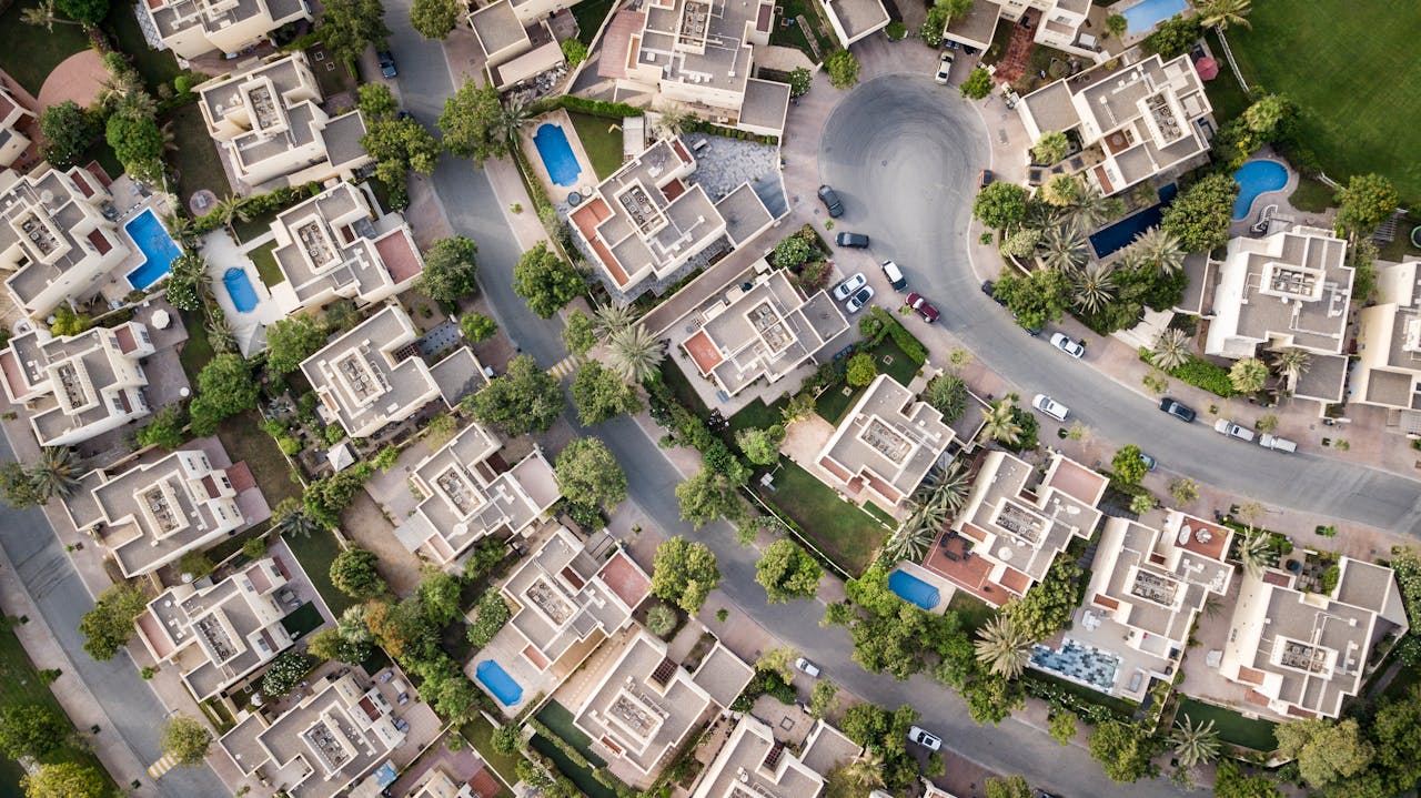 about-us Explore a stunning aerial view of a residential area in Dubai with lush greenery and swimming pools.